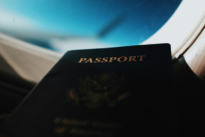 Un primo piano di un passaporto con un finestrino aereo che affaccia sull'ala, sullo sfondo. Il passaporto è un requisito indispensabile per la richiesta e la validità dell'ETA per il Regno Unito.